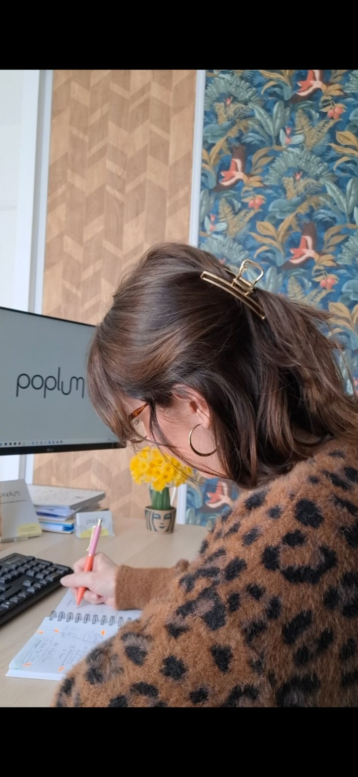 Julie, graphiste chez POPLUM, écrivant dans un carnet devant son ordinateur