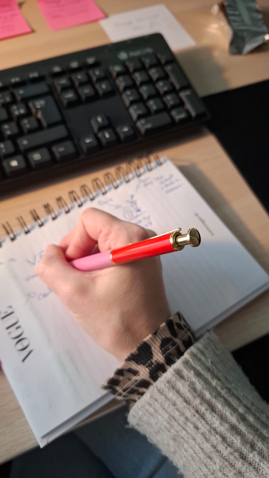 Main d’une graphiste annotant un carnet avec un stylo rouge devant son ordinateur